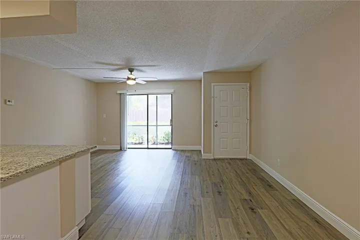 Unfurnished living room with a textured ceiling, dark wood finished floors, and ceiling fan
