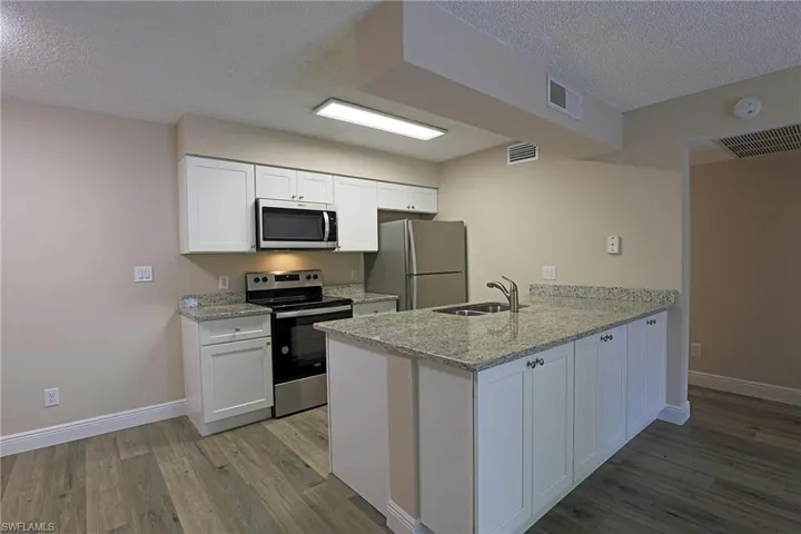 Kitchen with stainless steel appliances, light stone countertops, white cabinetry, a textured ceiling, and light wood-style floors