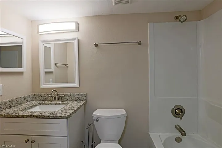 Full bathroom featuring vanity, a textured wall, and washtub / shower combination