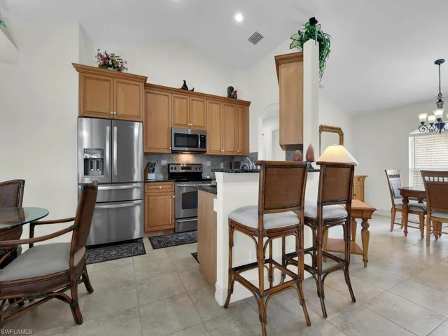 Kitchen with appliances with stainless steel finishes, dark countertops, decorative backsplash, brown cabinetry, and a breakfast bar area