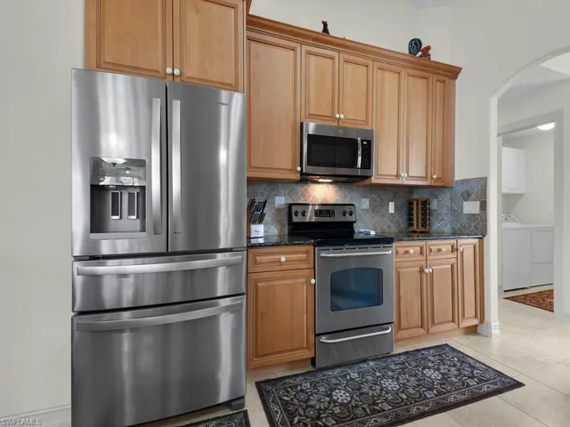 Kitchen featuring stainless steel appliances, arched walkways, decorative backsplash, dark stone counters, and washing machine and dryer