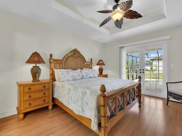 Bedroom featuring french doors, a tray ceiling, access to exterior, light wood-style flooring, and crown molding