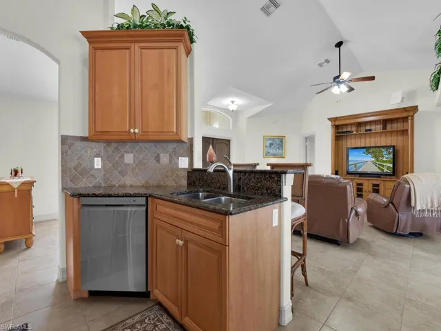 Kitchen with dishwasher, a sink, open floor plan, a ceiling fan, and a kitchen breakfast bar