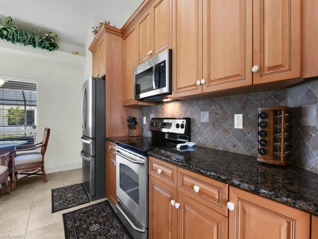 Kitchen featuring stainless steel appliances, decorative backsplash, dark stone counters, baseboards, and light tile patterned floors