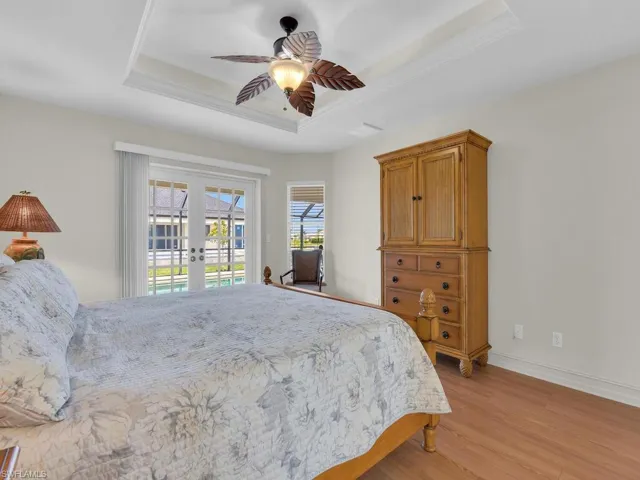 Bedroom featuring french doors, a tray ceiling, access to exterior, light wood-style flooring, and baseboards
