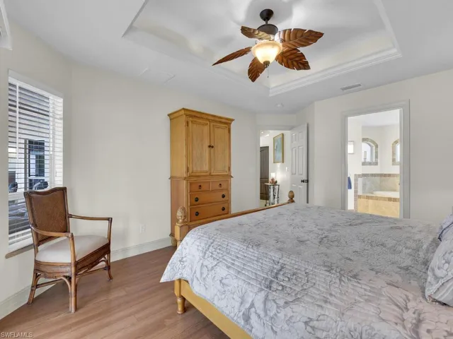 Bedroom featuring a tray ceiling, light wood-style flooring, multiple windows, and baseboards