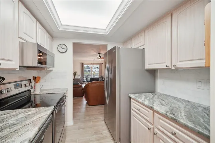 Kitchen featuring decorative backsplash, stainless steel appliances, light stone counters, and ceiling fan