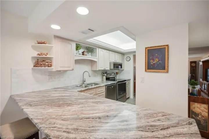Kitchen featuring kitchen peninsula, appliances with stainless steel finishes, tasteful backsplash, sink, and white cabinets