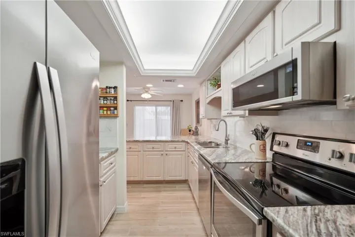 Kitchen featuring white cabinetry, sink, light stone countertops, a raised ceiling, and appliances with stainless steel finishes