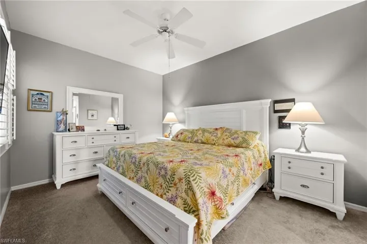 Bedroom featuring a vaulted ceiling with a ceiling fan, white plantation shutters, and soft gray wall paint