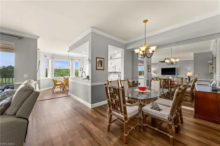 Open concept living space featuring wood-finish flooring, a contemporary chandelier, a mirrored wall, and crown molding