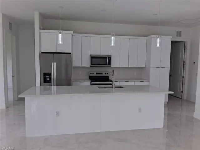 Kitchen featuring appliances with stainless steel finishes, white cabinetry, an island with sink, modern cabinets, and decorative light fixtures