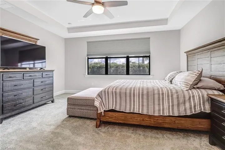 Carpeted bedroom with a raised ceiling and ceiling fan