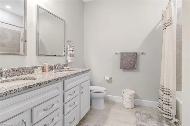 Full bathroom with tile flooring, double sink, shower / bathtub combination with curtain, toilet, and large vanity