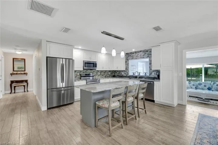 Kitchen featuring stainless steel appliances, light stone countertops, a kitchen island, a kitchen bar, and white cabinetry