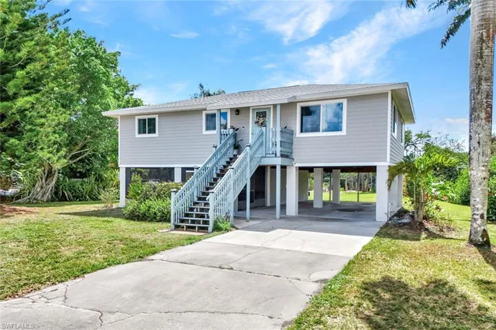 Coastal home with a front yard, a carport, concrete driveway, and a shingled roof
