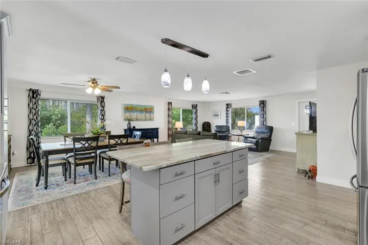Kitchen with open floor plan, a kitchen island, gray cabinets, light stone counters, and a kitchen bar