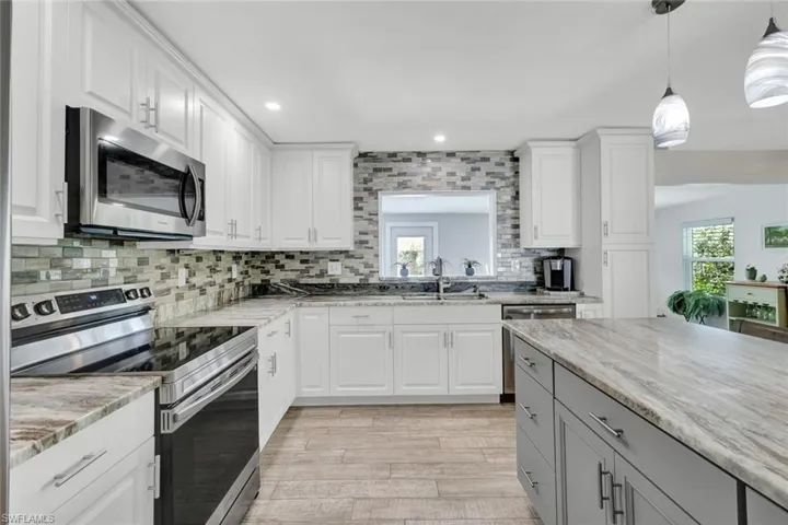 Two tone kitchen featuring stainless steel appliances, dual tone cabinetry, tasteful backsplash, decorative light fixtures, and light wood-style floors
