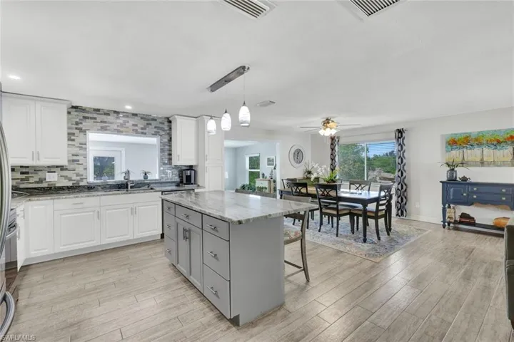Dual tone kitchen with two tone color scheme, decorative backsplash, a kitchen island, decorative light fixtures, and a kitchen breakfast bar