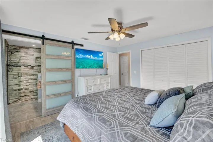 Bedroom with a barn door, light wood-style flooring, ensuite bathroom, a ceiling fan, and a closet