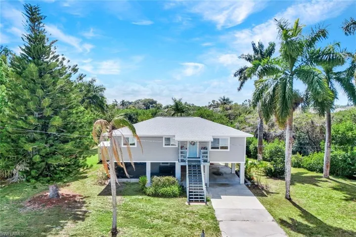 View of front of home featuring a front yard, driveway, a carport, and view of scattered trees
