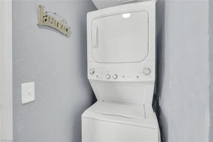 Laundry area with a textured wall and stacked washer and clothes dryer