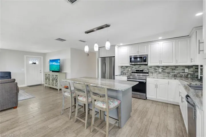 Kitchen with stainless steel appliances, open floor plan, light stone countertops, and white cabinets