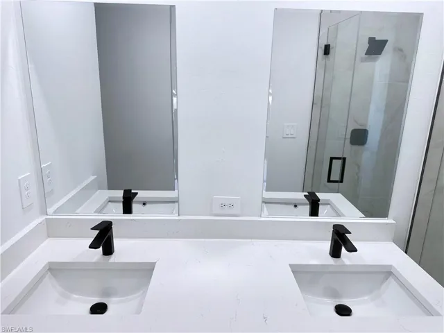 Full bath featuring a marble finish shower and double vanity