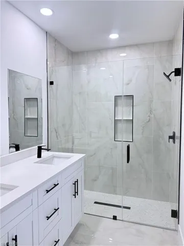 Full bath with a marble finish shower, double vanity, light marble finish flooring, and recessed lighting