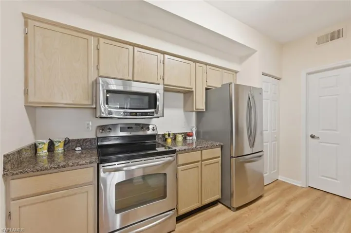 Kitchen with stainless steel appliances, light wood finish cabinets, light wood-type flooring, and dark stone countertops