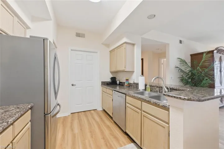 Kitchen with light wood finish cabinets, stainless steel appliances, a peninsula, light wood-style flooring, and dark stone countertops