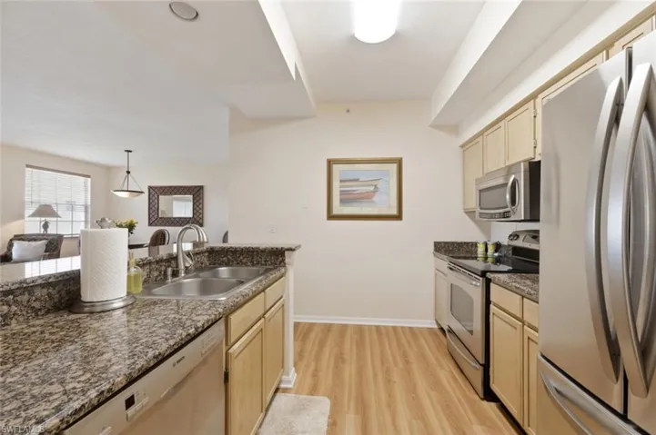 Kitchen featuring stainless steel appliances, light wood finish cabinets, light wood-style floors, hanging light fixtures, and dark stone countertops