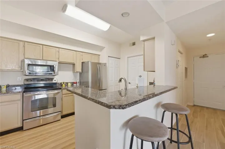 Kitchen with a kitchen bar, stainless steel appliances, light wood finished floors, a peninsula, and light wood finish cabinetry