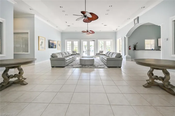 Living room with a ceiling fan, french doors, arched walkways, light tile patterned flooring, and crown molding