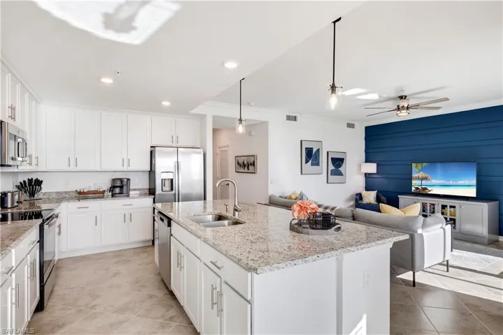 Kitchen with ceiling fan, an island with sink, sink, white cabinetry, and appliances with stainless steel finishes