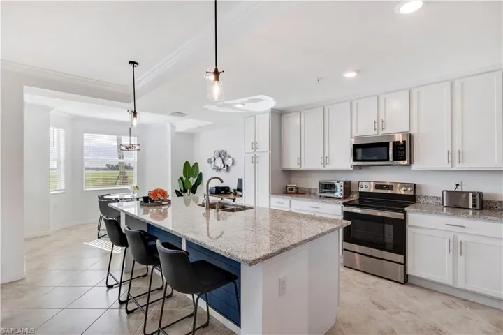 Kitchen with an island with sink, pendant lighting, sink, white cabinets, and appliances with stainless steel finishes