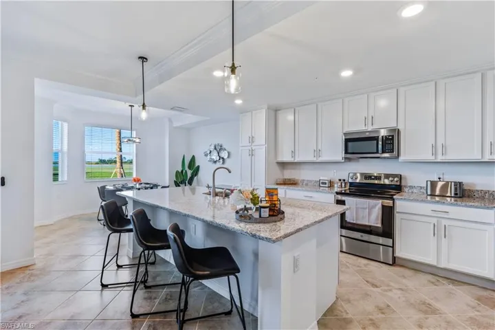 Kitchen featuring white cabinetry, a center island with sink, appliances with stainless steel finishes, decorative light fixtures, and light tile floors