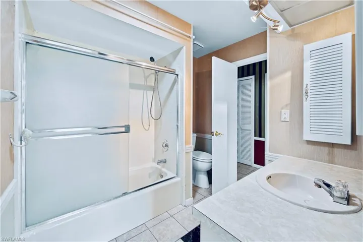 Full bathroom featuring shower / bath combination with glass door, vanity, tile patterned floors, and toilet