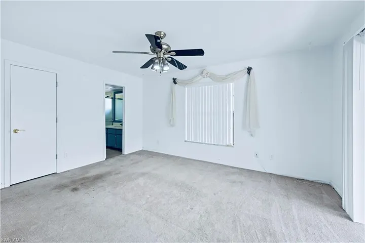 Unfurnished bedroom featuring light carpet, ensuite bathroom, and ceiling fan