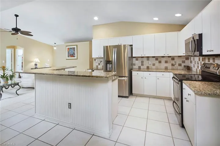 Kitchen featuring stainless steel appliances, backsplash, lofted ceiling, white cabinets, and light stone counters
