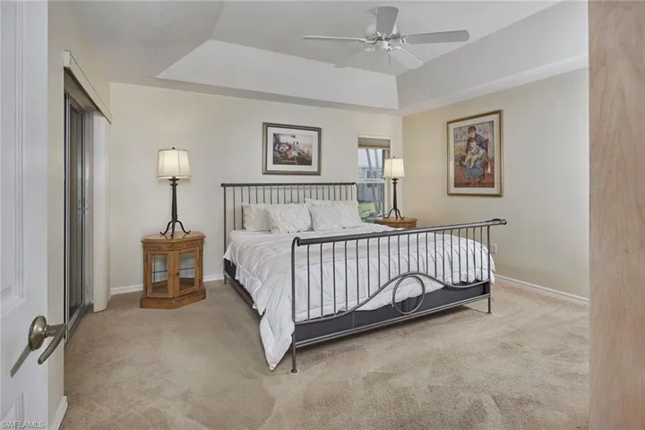 Bedroom featuring a raised ceiling, light colored carpet, and a ceiling fan