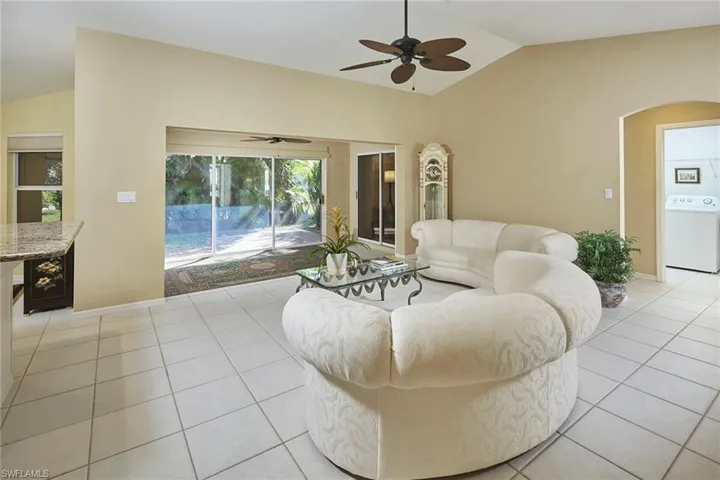 Living room featuring lofted ceiling, washer / clothes dryer, light tile patterned floors, arched walkways, and ceiling fan