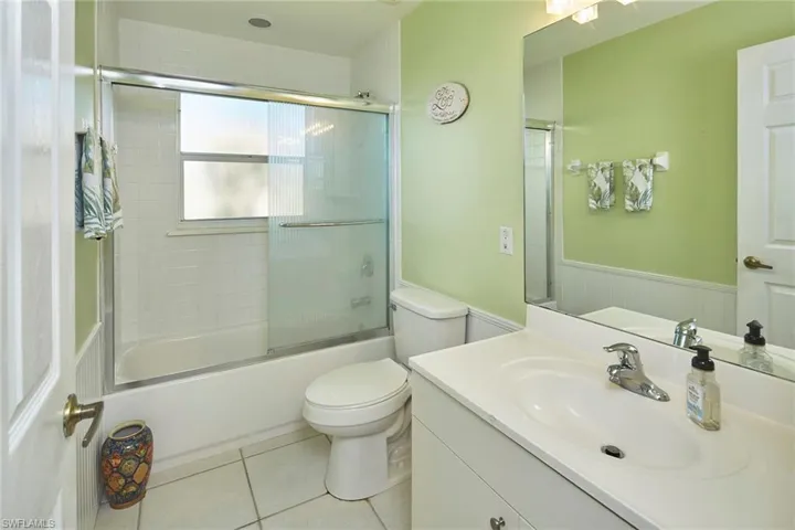 Full bathroom featuring vanity, combined bath / shower with glass door, light tile patterned floors, and wainscoting
