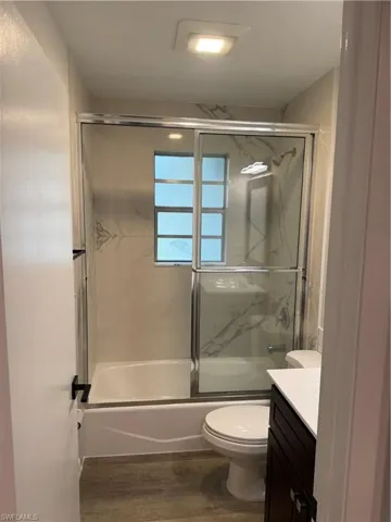 Bathroom with vanity, bath / shower combo with glass door, and dark wood finished floors