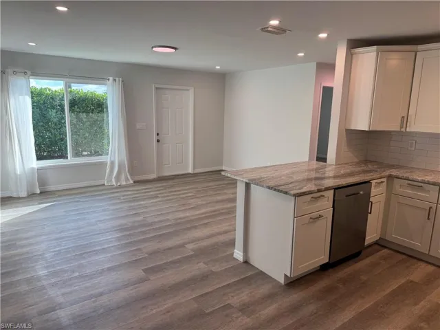Kitchen featuring white cabinets, light stone countertops, recessed lighting, stainless steel dishwasher, and a peninsula
