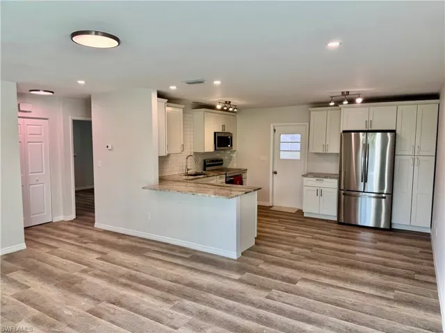 Kitchen with appliances with stainless steel finishes, white cabinets, light stone counters, recessed lighting, and a peninsula