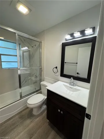 Bathroom with vanity, shower / bath combination with glass door, and dark wood-style floors