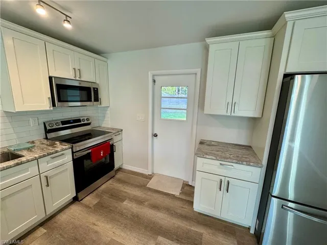 Kitchen with appliances with stainless steel finishes, white cabinetry, and light stone counters