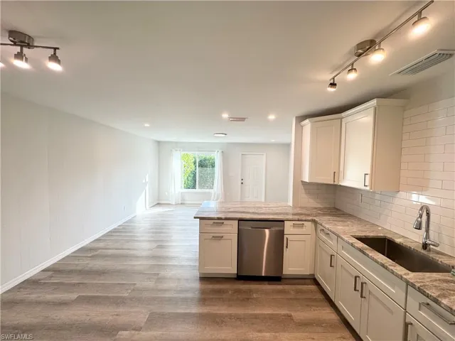 Kitchen featuring backsplash, light stone counters, dishwasher, and a peninsula