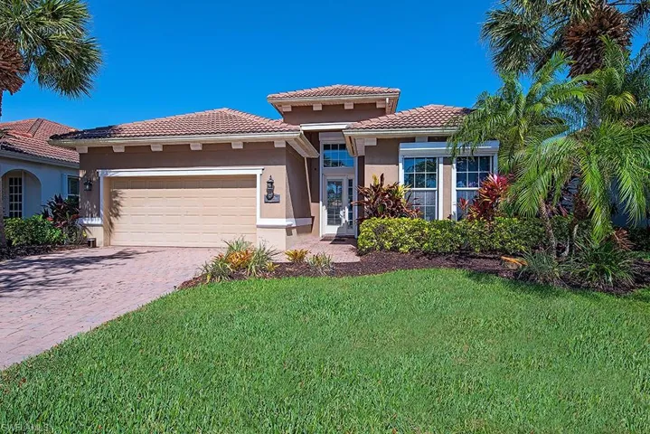 Mediterranean / spanish-style house with a garage, driveway, stucco siding, a tile roof, and a front lawn